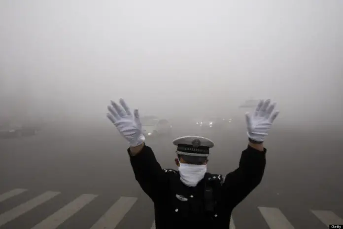 2013年10月21日，中国东北黑龙江省哈尔滨市，一名警察在雾霾弥漫的街道上工作时做手势。报道称，令人窒息的污染云笼罩了哈尔滨，哈尔滨以一年一度的冰雪节而闻名，能见度降至10米(33英尺)，突显出中国面临的环境挑战。CHINA OUT法新社图片(图片来源应为STR/AFP/Getty Images)